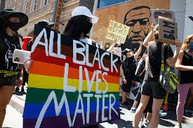 All Black Lives Matter protesters hold rainbow-colored signs near a mural of George Floyd during their solidarity march with the LGBTQ community in Los Angeles.

